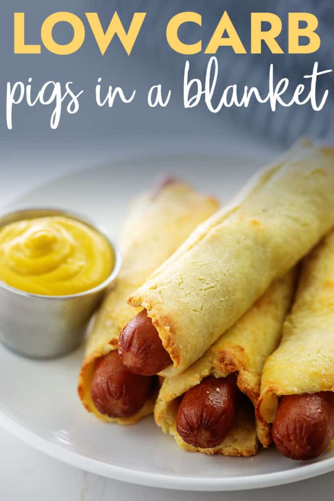 pigs in a blanket on white plate with mustard.