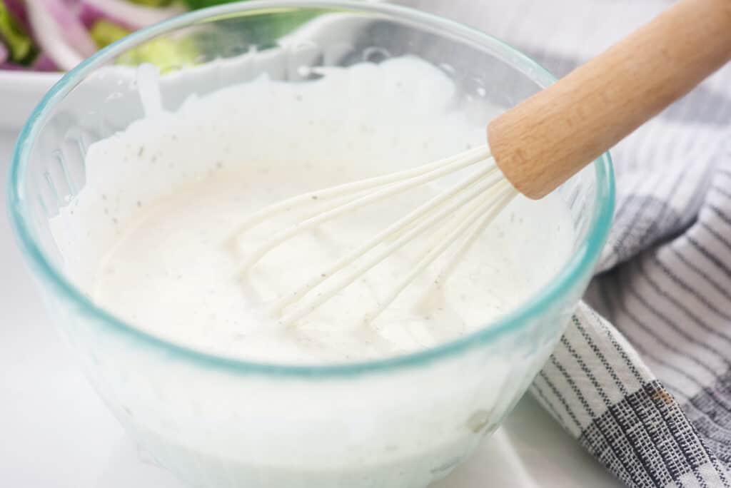 tzatziki salad dressing in glass bowl with whisk.