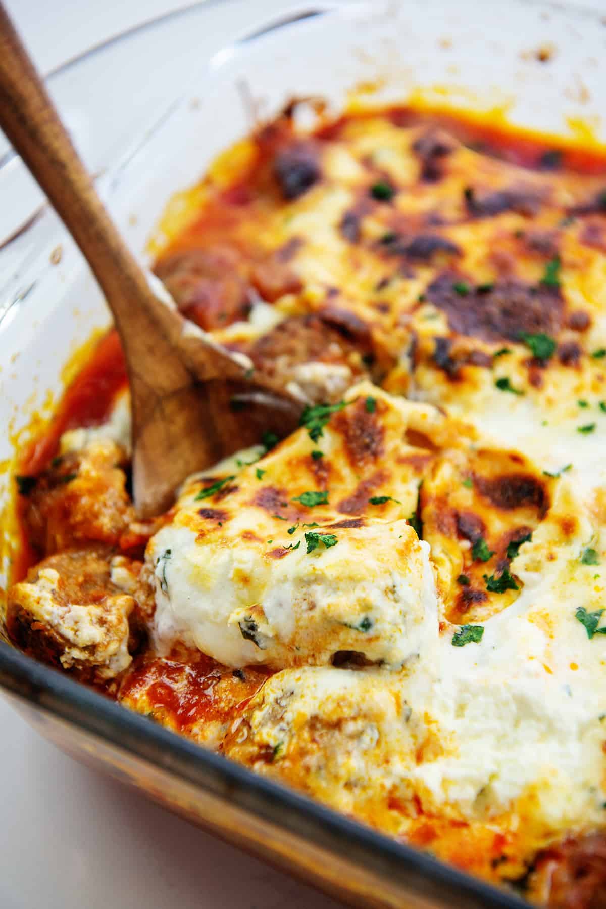 spoon full of cheesy meatballs in glass baking dish.