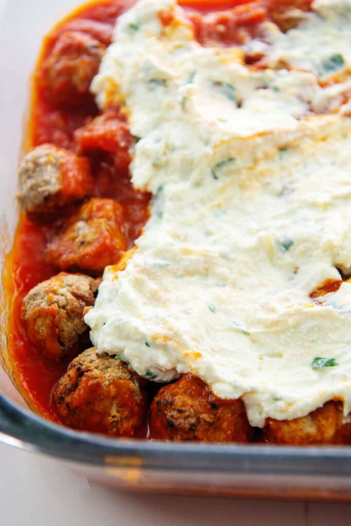 meatballs in baking dish topped with ricotta cheese mixture.