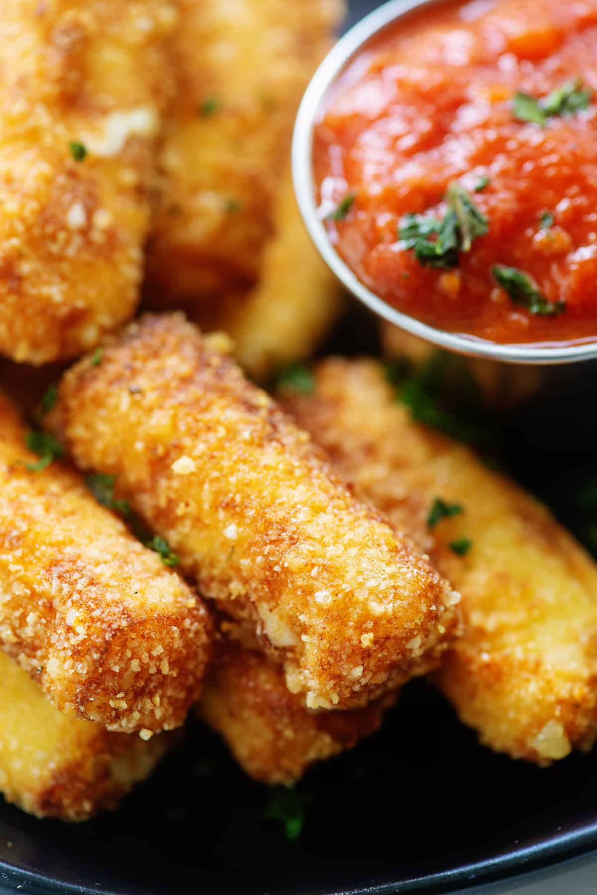 Keto mozzarella sticks on black plate next to marinara.