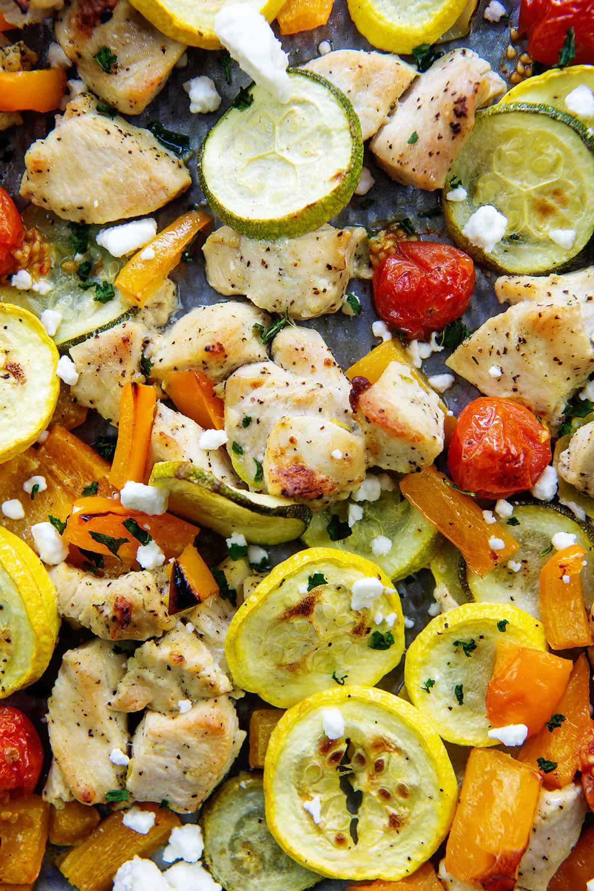 overhead view of greek chicken and vegetables on a sheet pan.