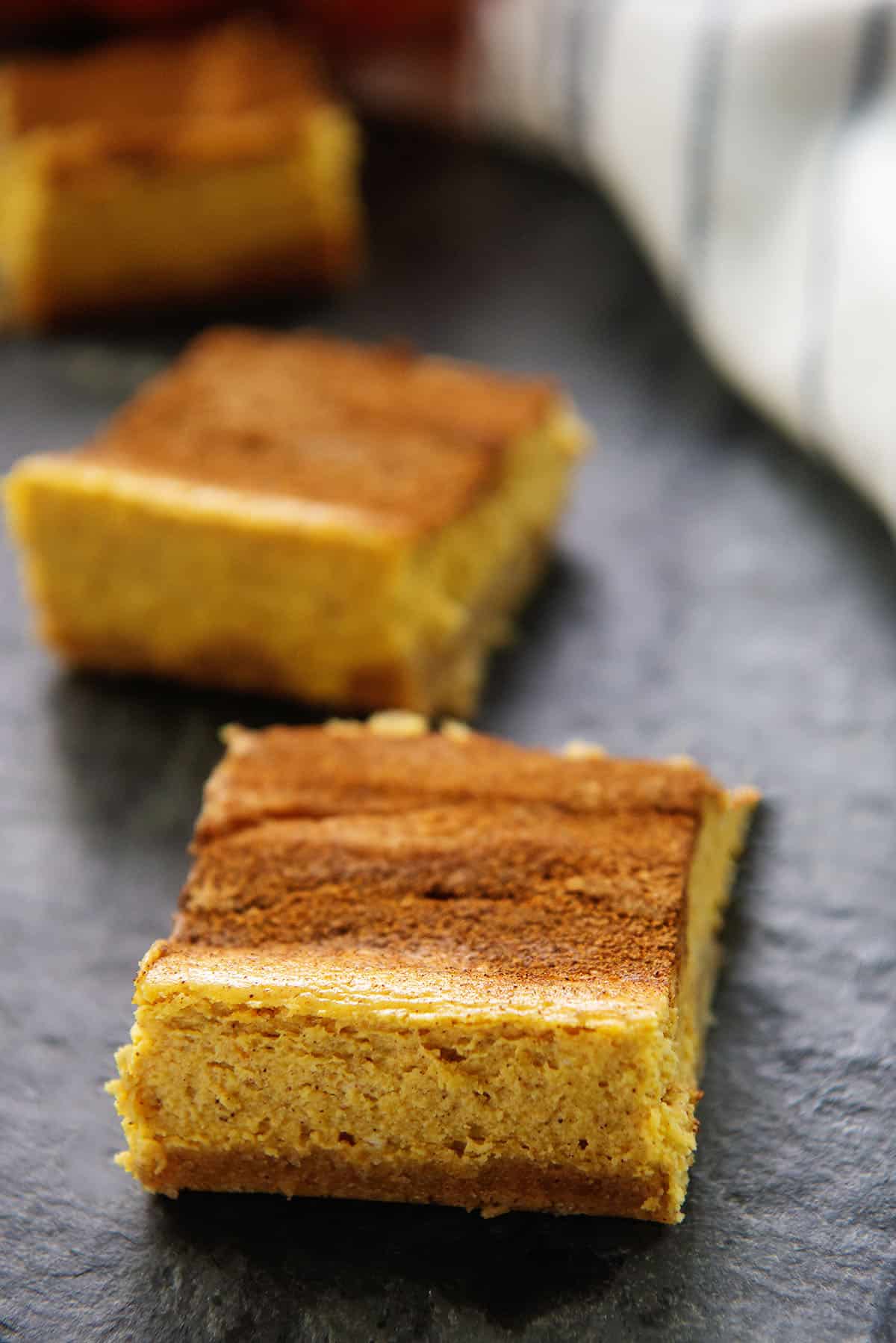 keto pumpkin cheesecake bars on black background.