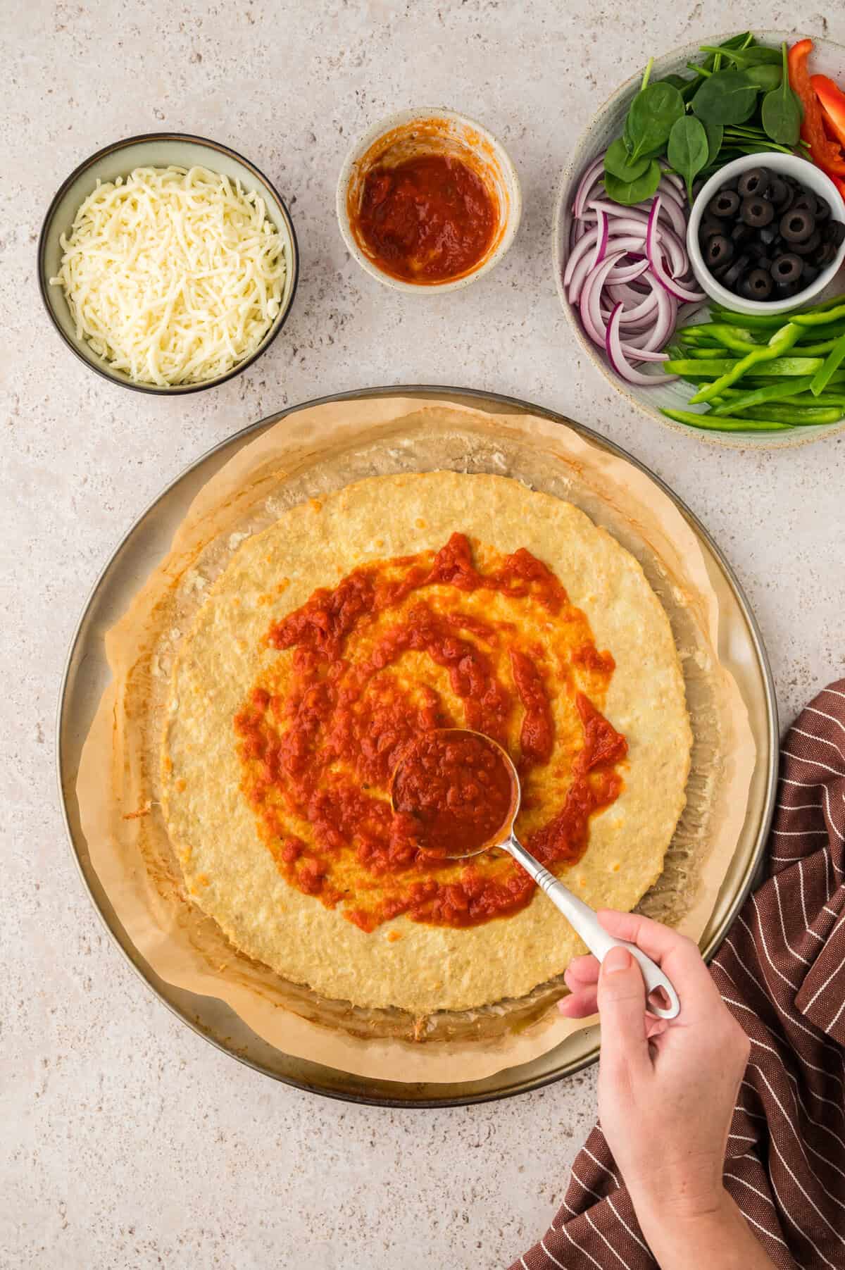 Chicken crust pizza being spread with marinara.