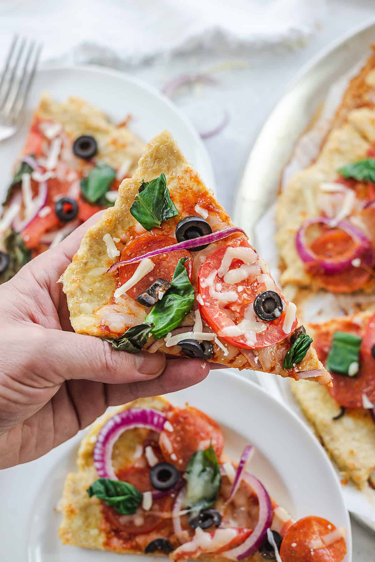 hand holding a slice of chicken crust pizza.