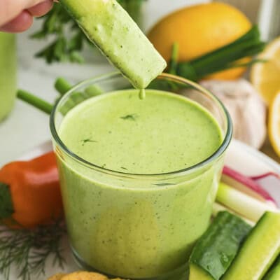 Green goddess dressing dripping off a cucumber.