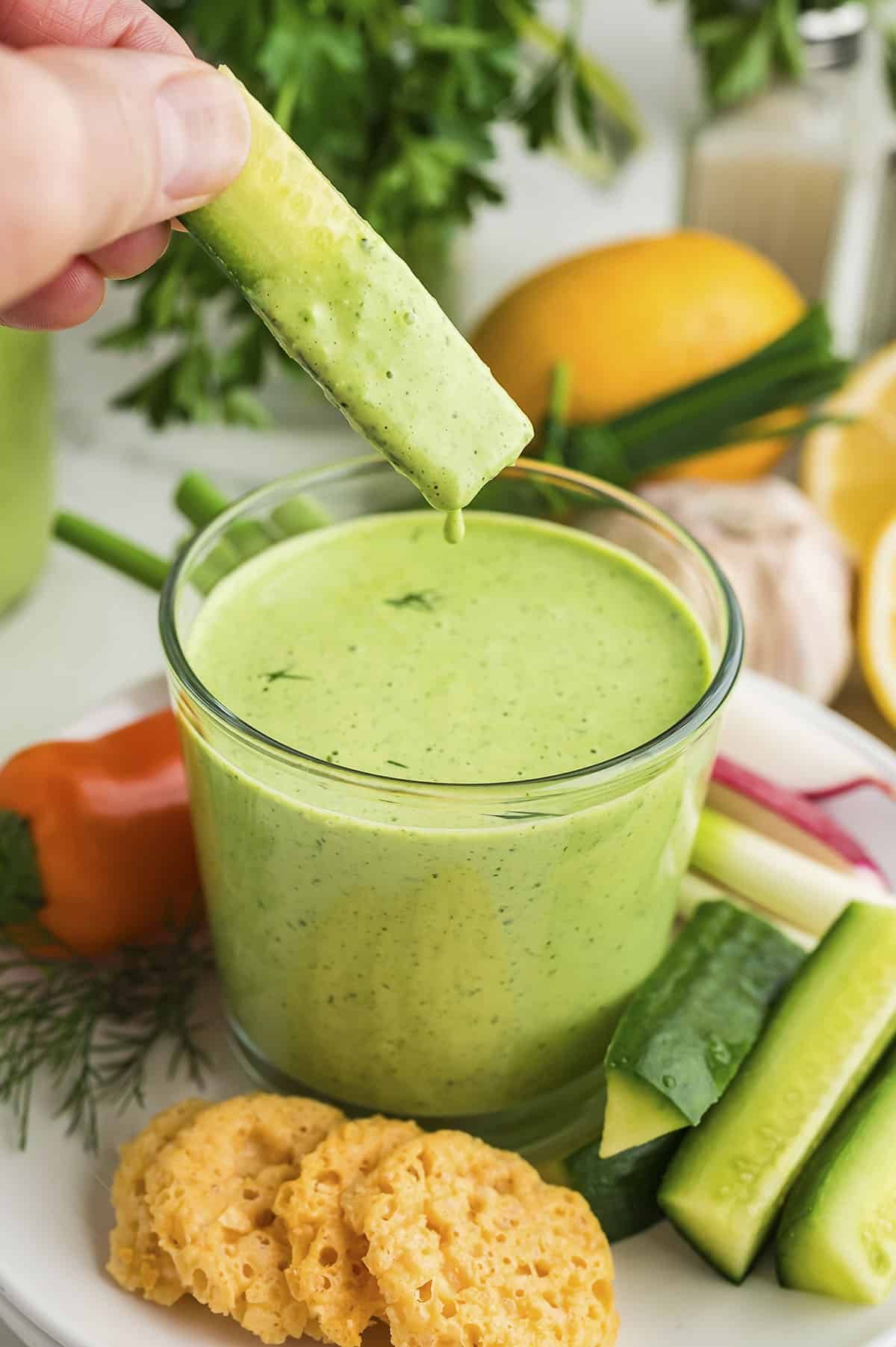 Green goddess dressing dripping off a cucumber.