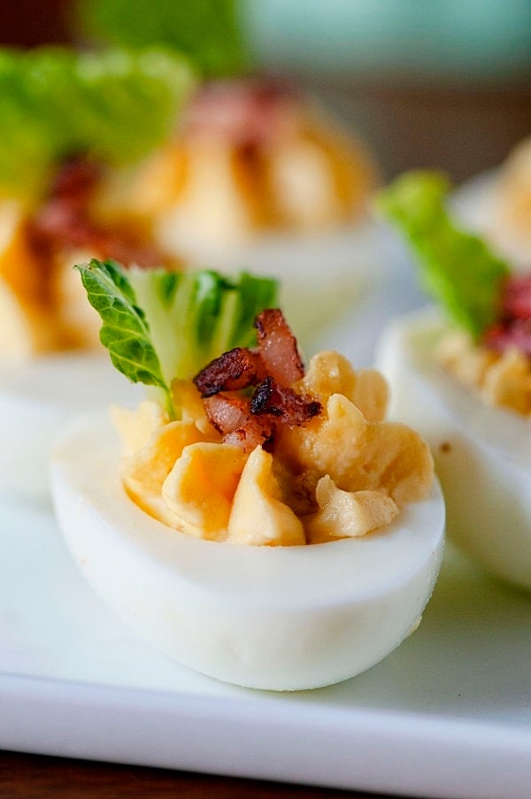A close up view of bacon caesar salad deviled eggs on a tray.
