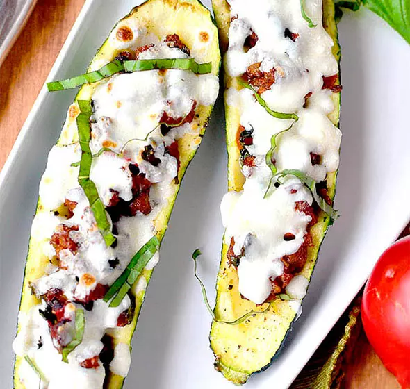 A top down view of a white dish with two Italian tomato basil stuffed zucchini boats.