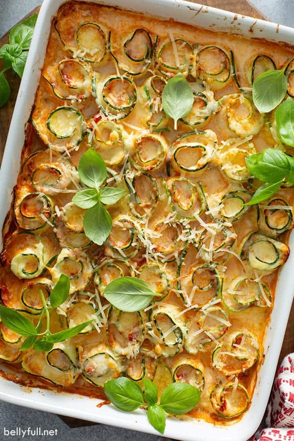 Zucchini lasagna rolls in a white baking dish with fresh herbs.