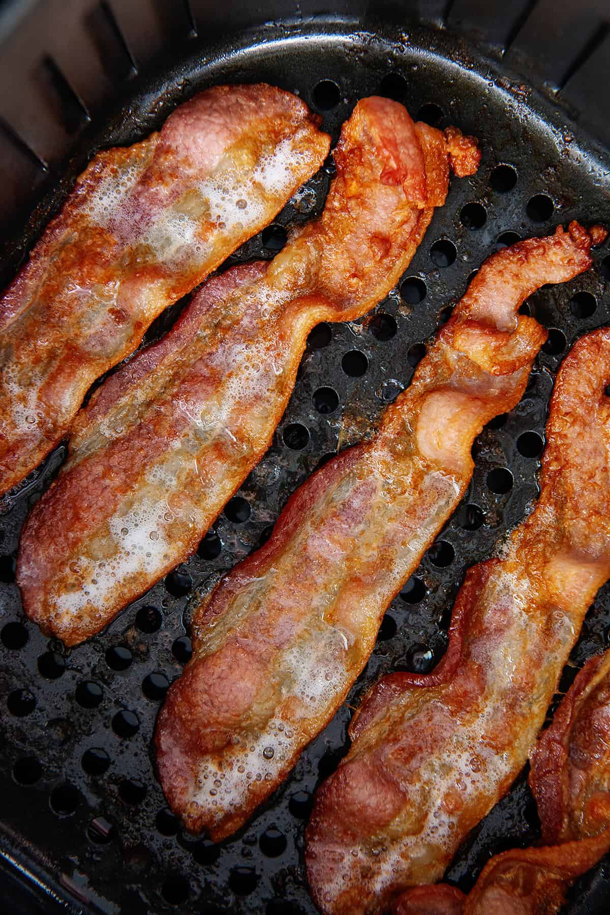 A top down view of an air fryer basket containing air fried bacon.