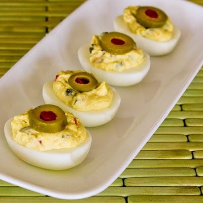 A white serving dish on a table with four green olive deviled eggs.