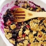 keto berry crisp in white dish with wooden spoon.