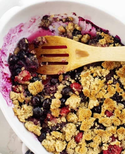 keto berry crisp in white dish with wooden spoon.