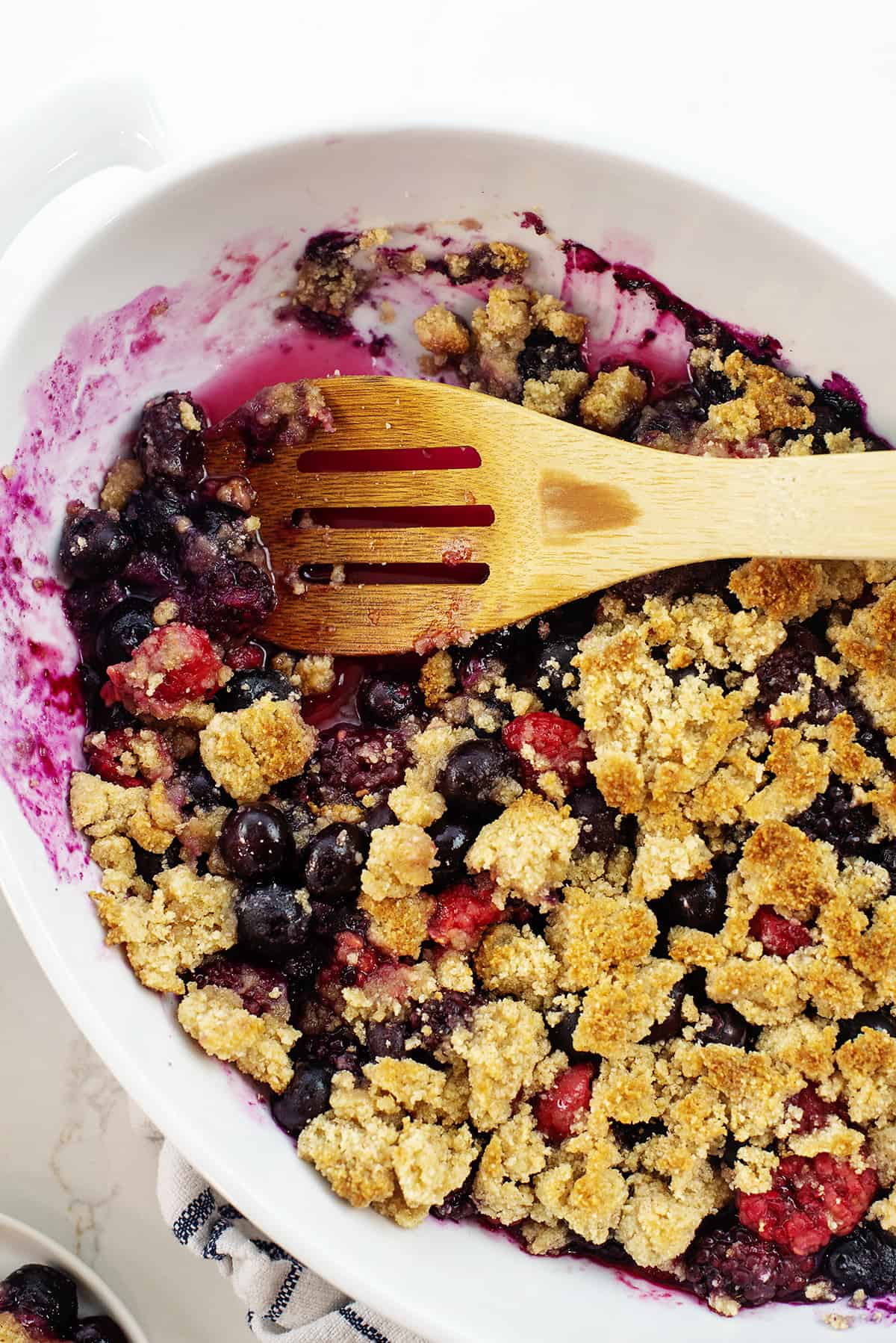 keto berry crisp in white dish with wooden spoon.