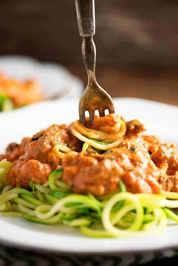 A close up view of low carb zoodles with sauce on a white plate with a fork stuck in the center.