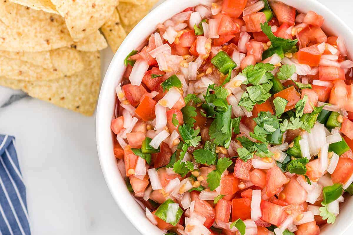 A top down view of pico de gallo in a white bowl next to chips.