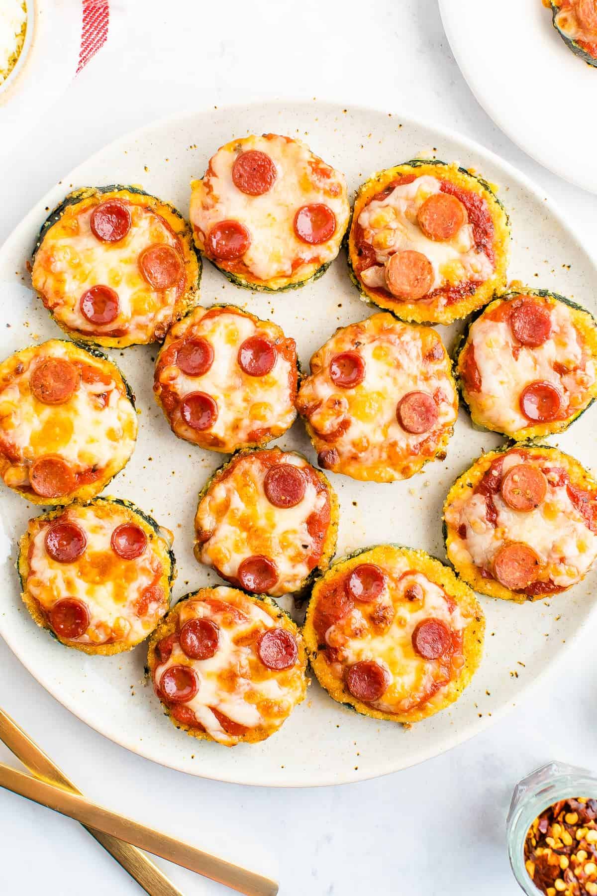 A top down view of a white plate containing zucchini pizza bites.
