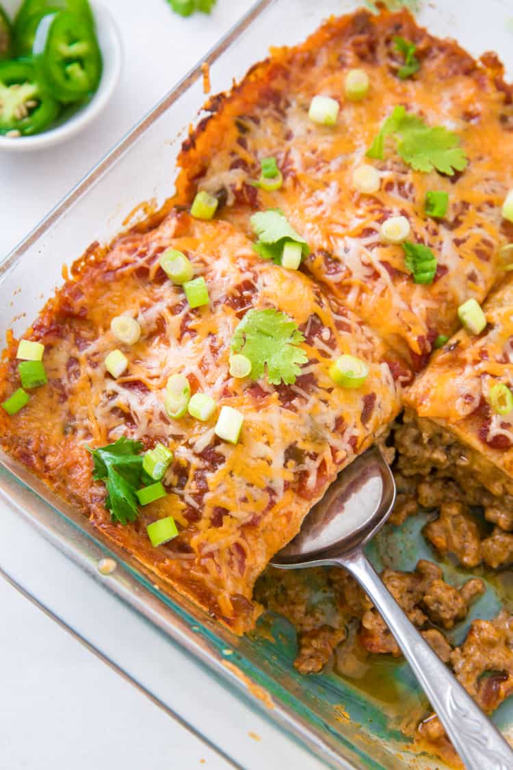 A glass baking dish containing sliced keto Mexican casserole with one slice removed and another being scooped out.