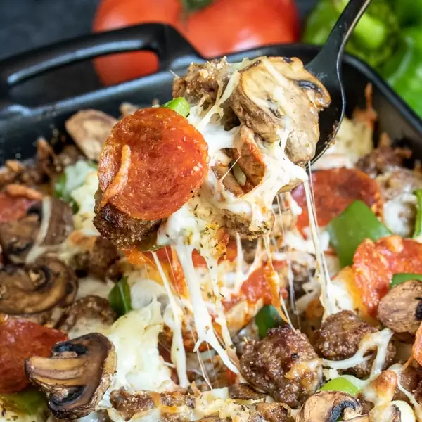 A forkful of low carb pizza casserole over the baking dish with the rest of the casserole.