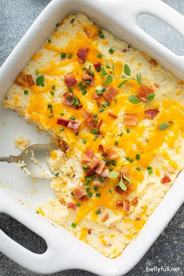 A white baking dish with mashed cauliflower with cheese and bacon, with a quarter of the casserole removed.