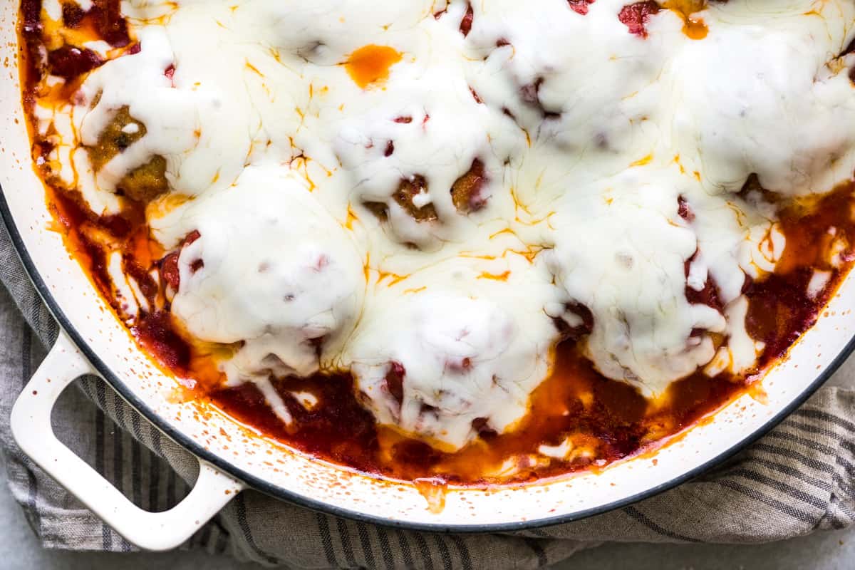 A white baking dish containing chicken parmesan meatballs covered in cheese and sauce.