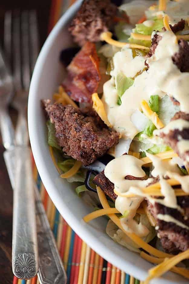 A top down view of a white bowl with keto bacon cheeseburger salad next to forks on a table.