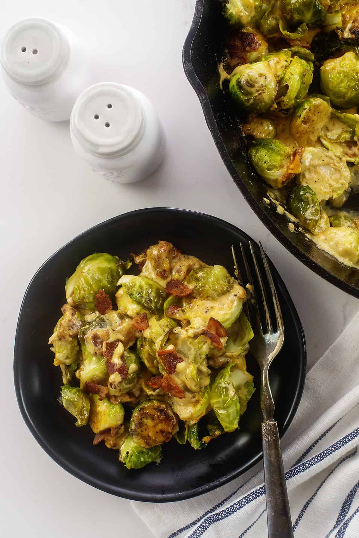Overhead view of Brussels sprouts casserole on black plate next to skillet.
