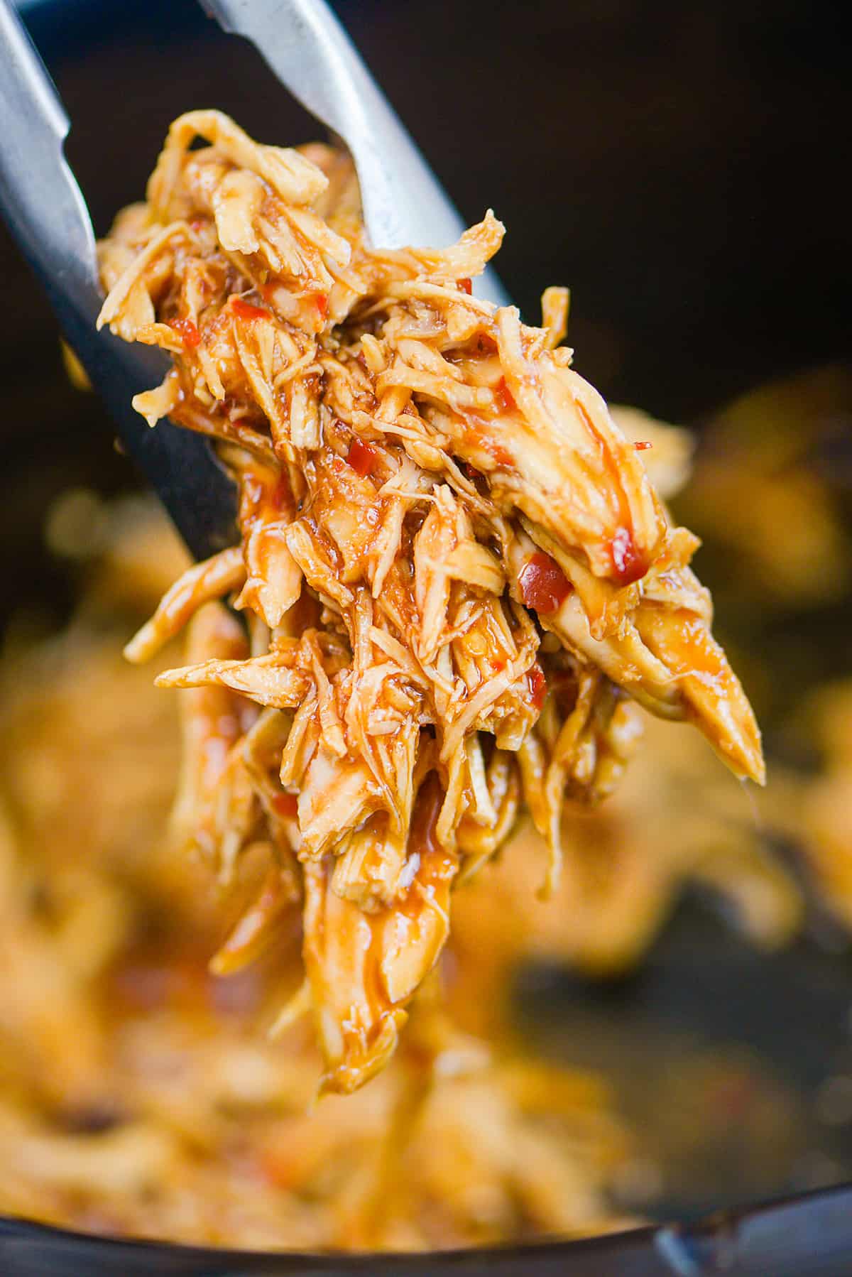 Shredded BBQ chicken in tongs over crockpot.