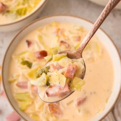 Bowl full of ham and cabbage soup on a spoon.