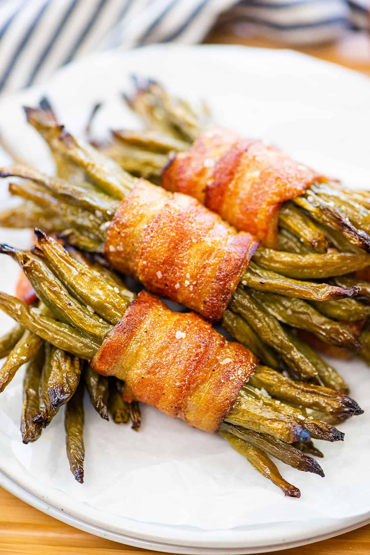 Green bean bundles wrapped in bacon on white plate.