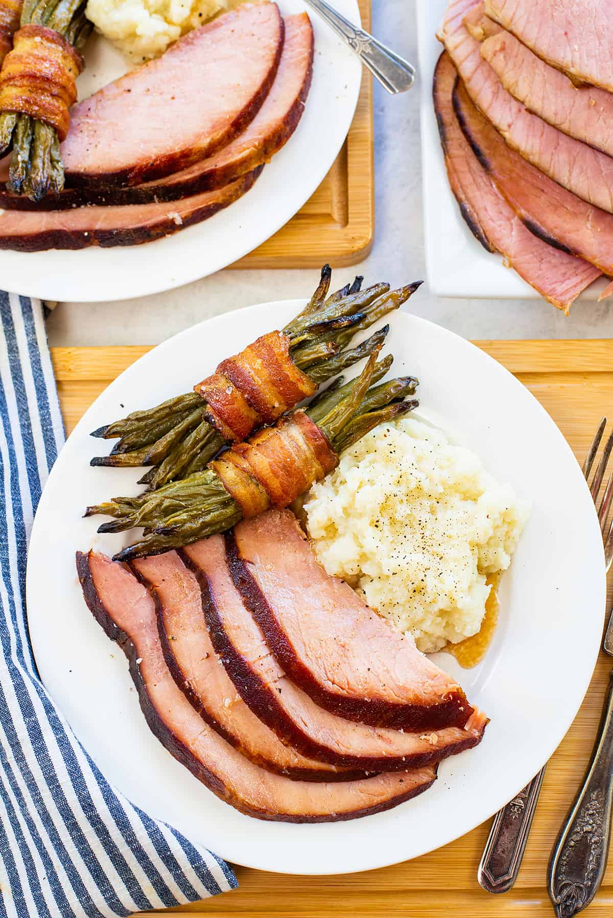 Slices of ham on plate next to mashed cauliflower and bacon wrapped green beans.