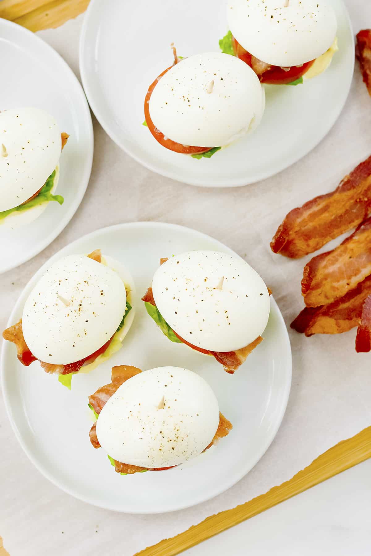 Boiled egg BLT sandwiches on white plates.