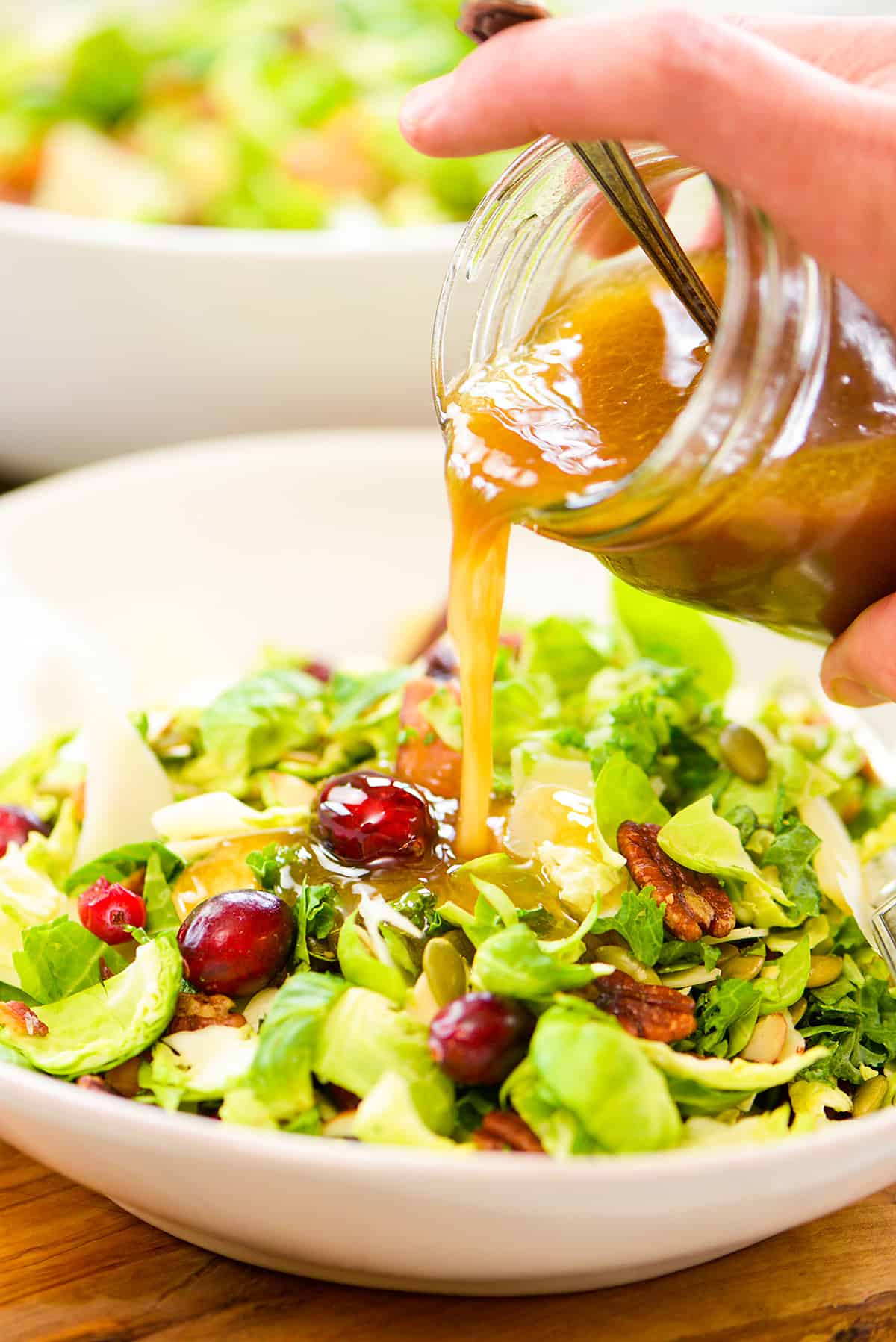 Maple dijon dressing being poured over brussels sprout kale salad.