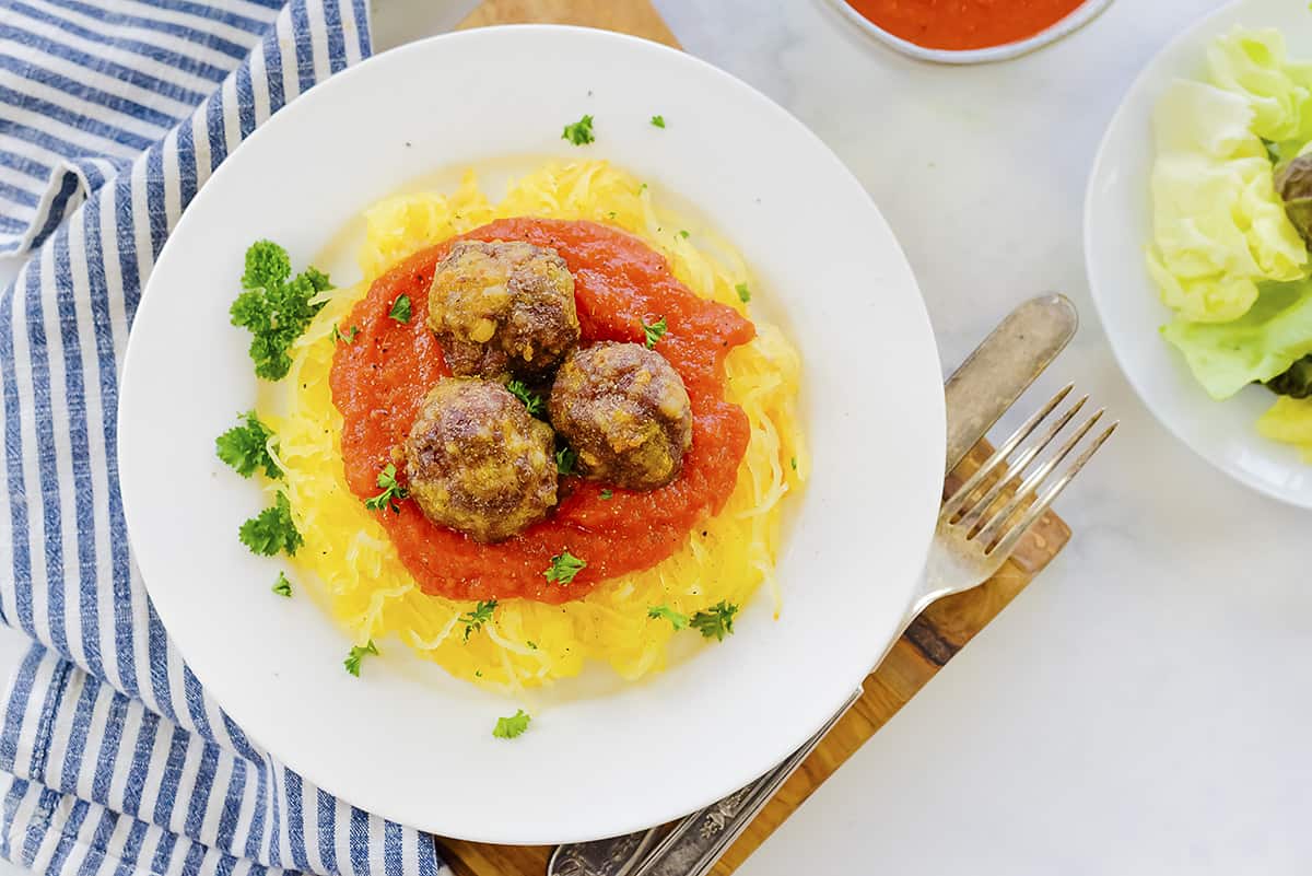 Overhead view of spaghetti squash with meatballs and marinara on plate.