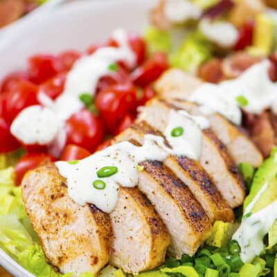 Sliced chicken on salad topped with ranch dressing.