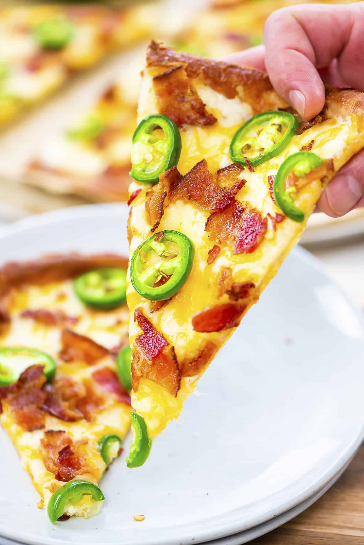 Hand holding a slice of jalapeno popper pizza.