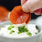 Hand dipping pepperoni chips in cream cheese.