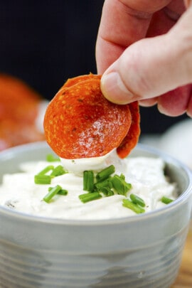 Hand dipping pepperoni chips in cream cheese.