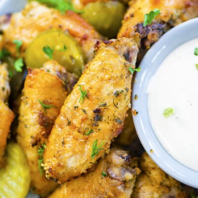 Baked ranch wings in bowl with pickles and ranch dressing.