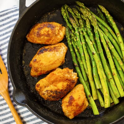 Cast iron skillet full of chicken thighs and cooked asparagus.