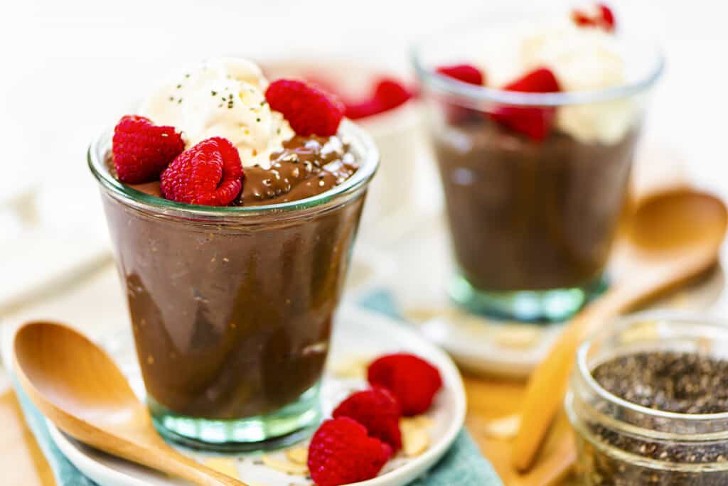 Keto chia pudding in jars topped with whipped cream and raspberries.