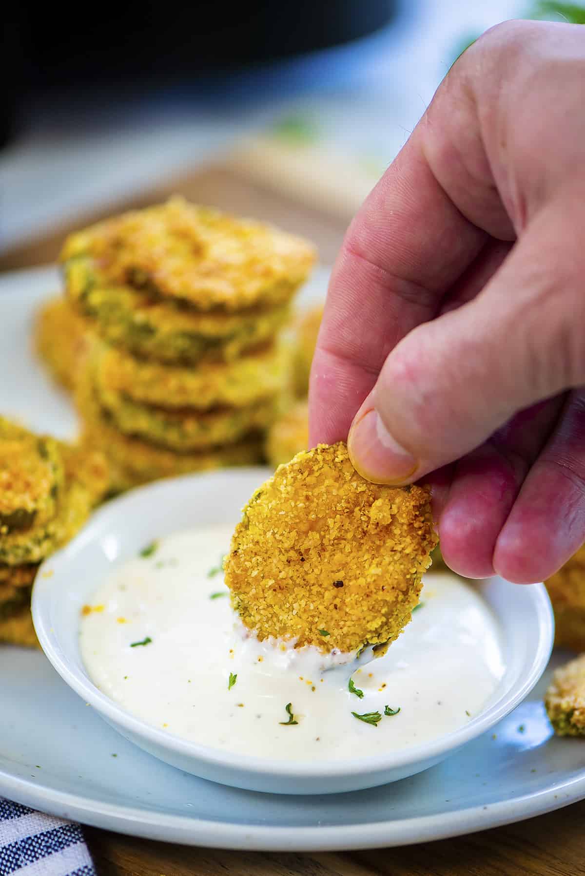 Hand dipping a pickle into ranch dressing.