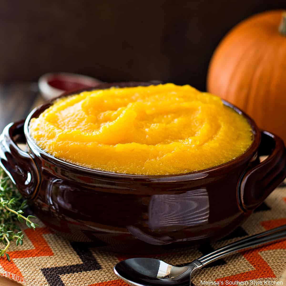 A bowl containing homemade pumpkin puree on a table next to a spoon and a pumpkin.