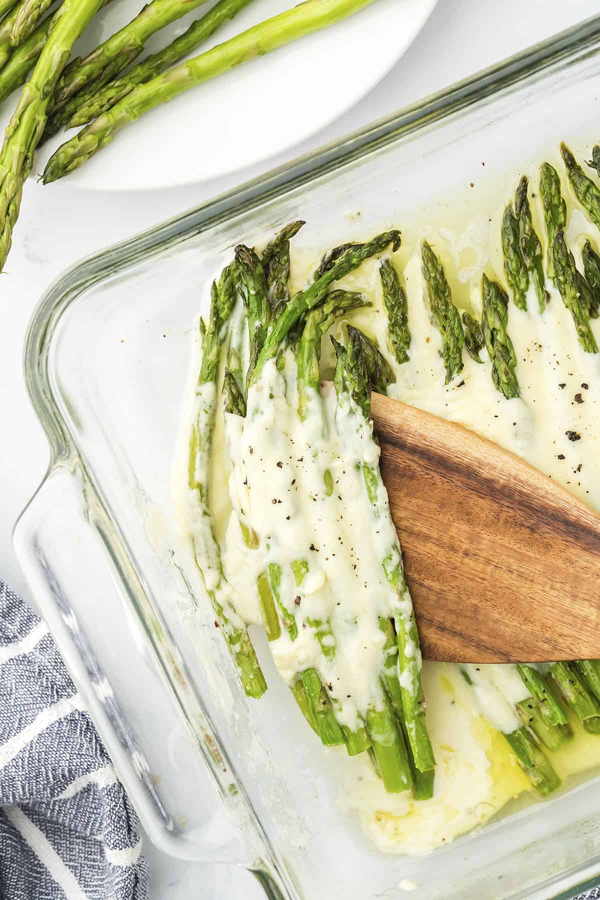 Baked asparagus topped with alfredo sauce in glass baking dish.