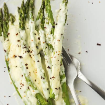 Alfredo baked asparagus on white plate with fork.