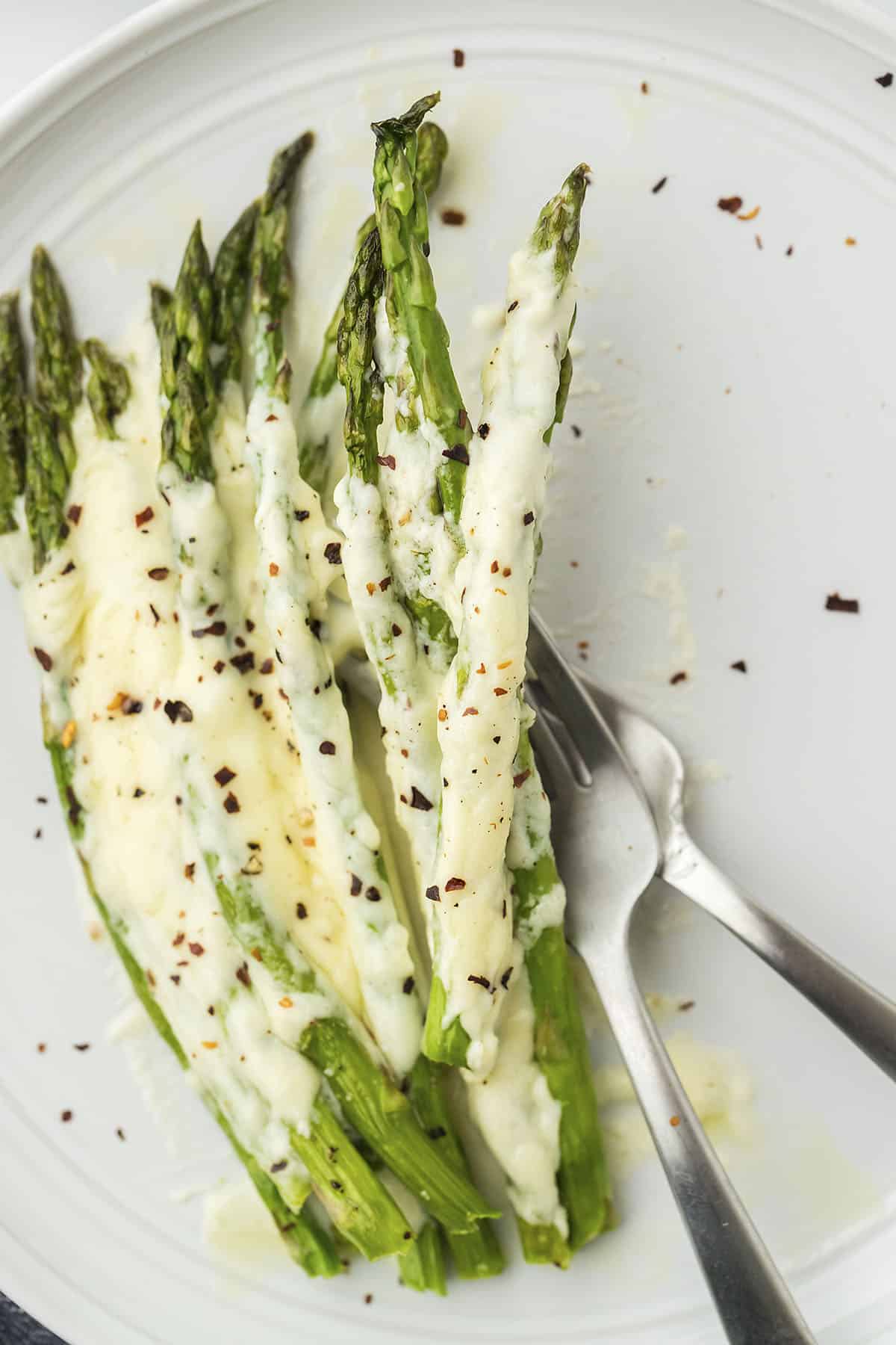 Alfredo baked asparagus on white plate with fork.