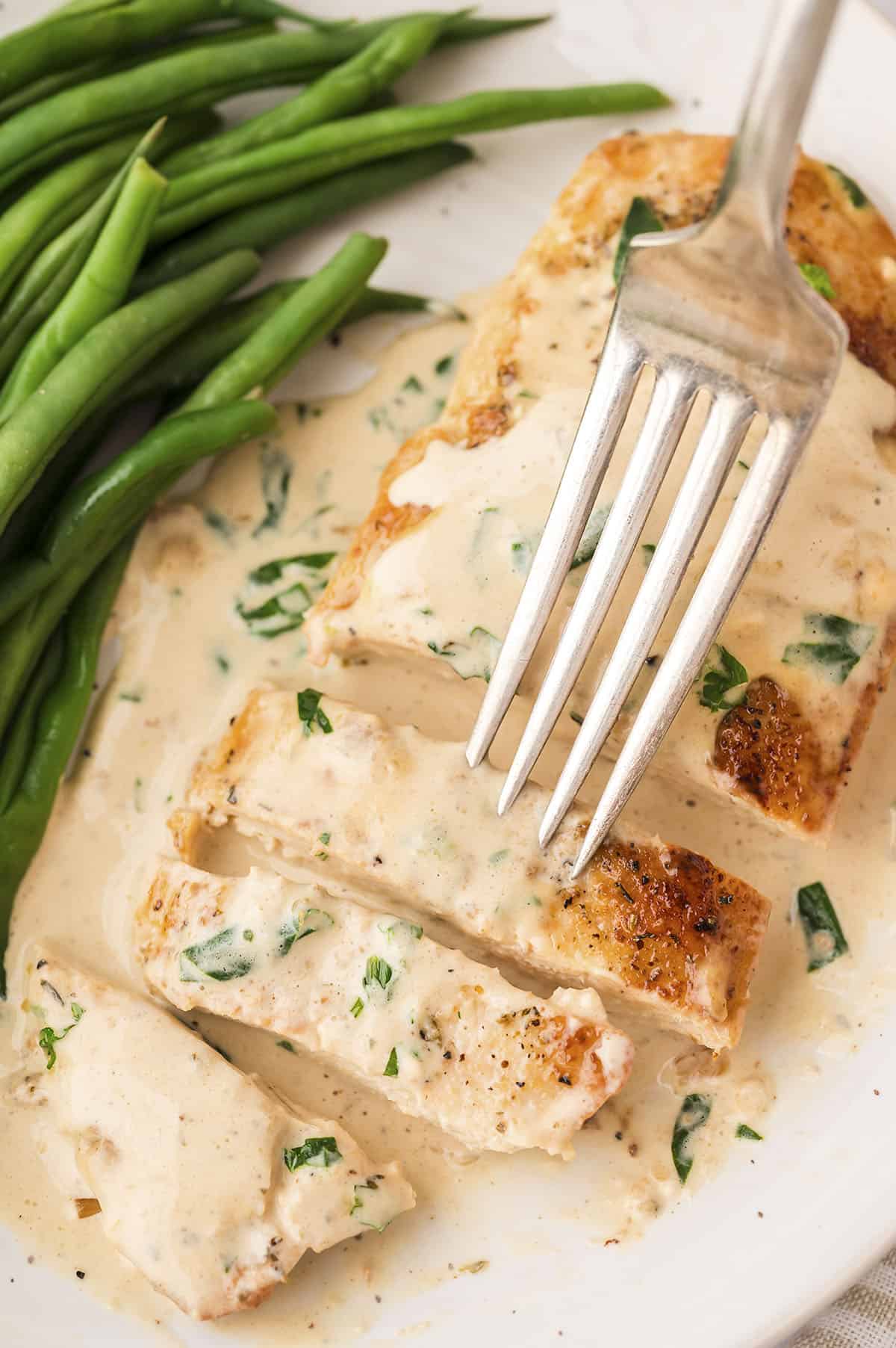 Sliced garlic parmesan chicken breast on white plate with fork.