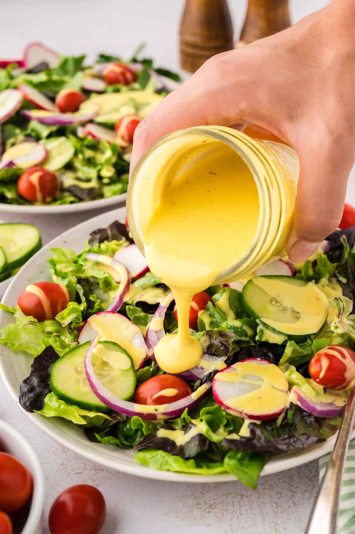 Keto honey mustard dressing being drizzled over a green salad.