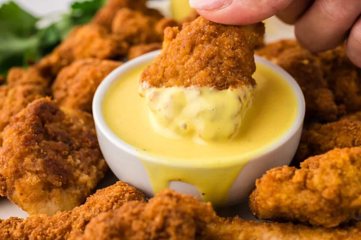 Chicken nugget being dipped in keto honey mustard.